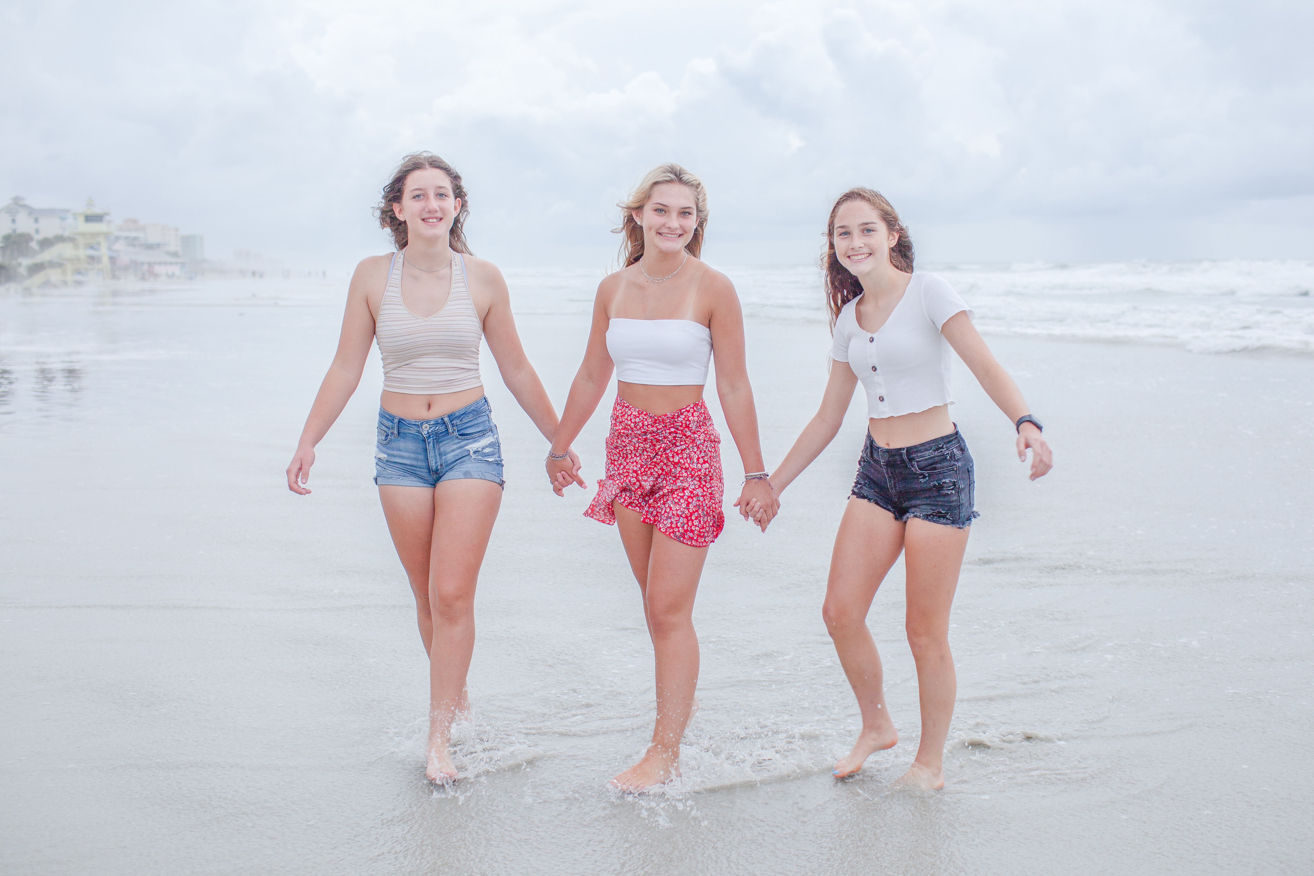 Girl best friends holding hands walking through the water at the beach.