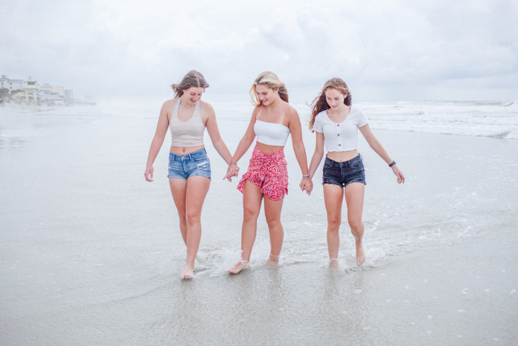 Three girl best friends taking a selfie with a phone propped on the stairs of the beach boardwalk in New Symrna Beach