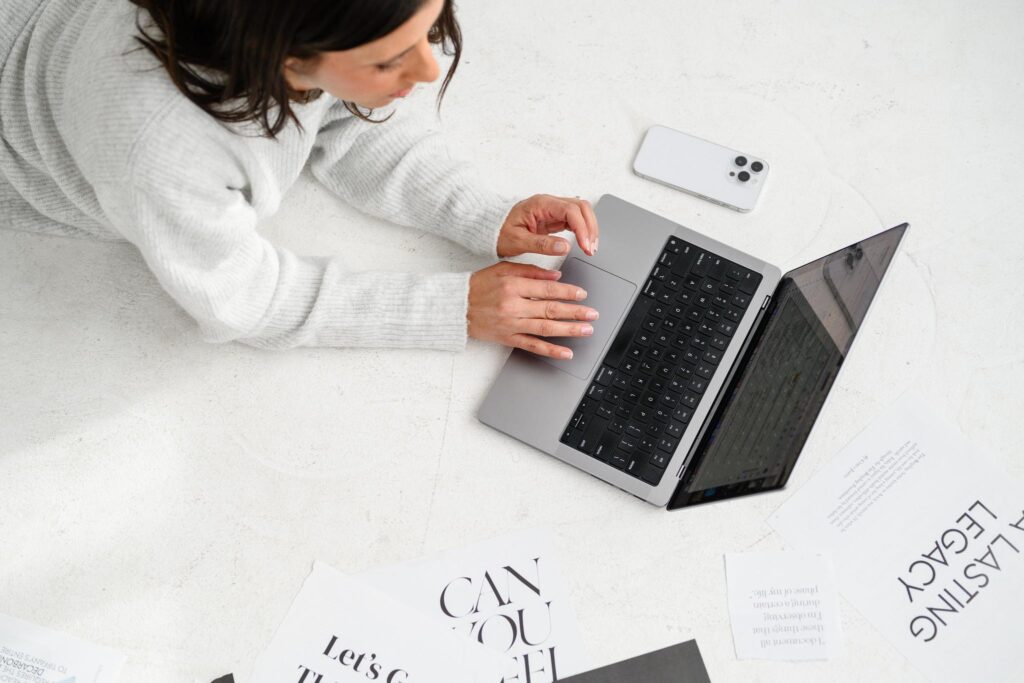 A woman laying on her stomach on the floor, typing on a laptop. She appears focused and comfortable while working.