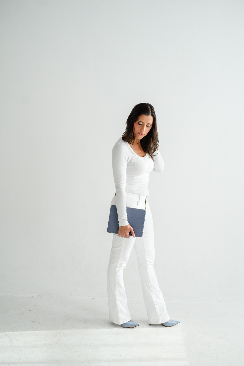 Confident woman in all-white outfit holding a navy tablet in a minimal white studio, showcasing modern personal branding.