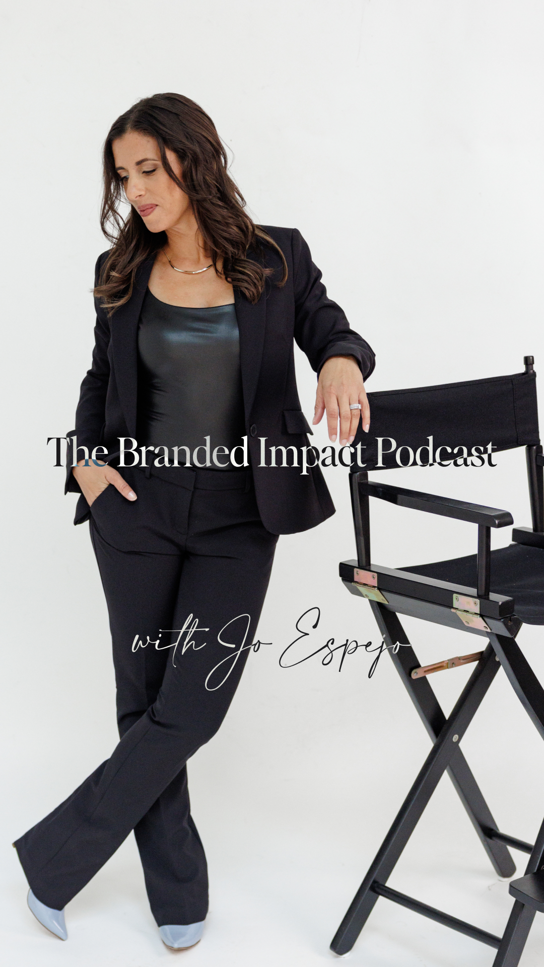 Jo Espejo, host of The Branded Impact Podcast, standing confidently next to a director’s chair in a black blazer and leather top, representing personal branding and business leadership.