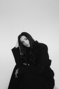Black and white portrait of Jordan Henderson in a dark oversized coat, guest on The Branded Impact Podcast