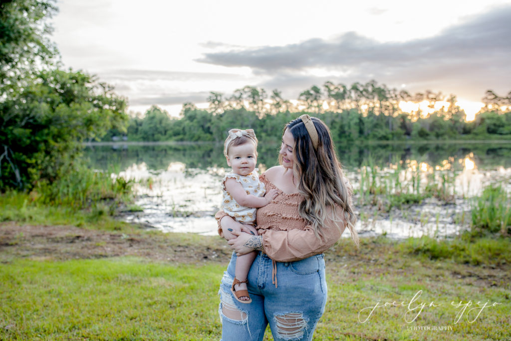 Mom holding her daughter in front of a lake at sunrise.