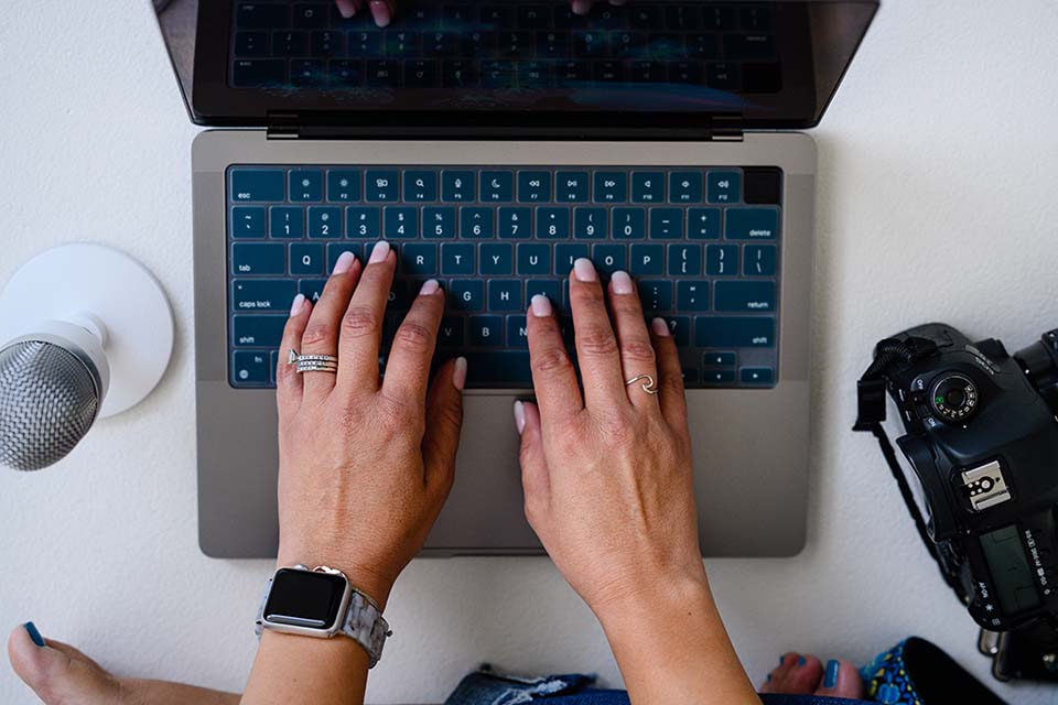 Woman typing on a keyboard, working on a laptop with branding photos displayed on the screen