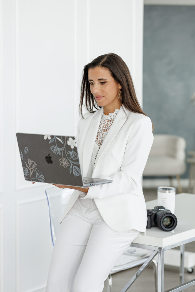Female branding strategist working on laptop in white office space with camera, planning visual brand strategy